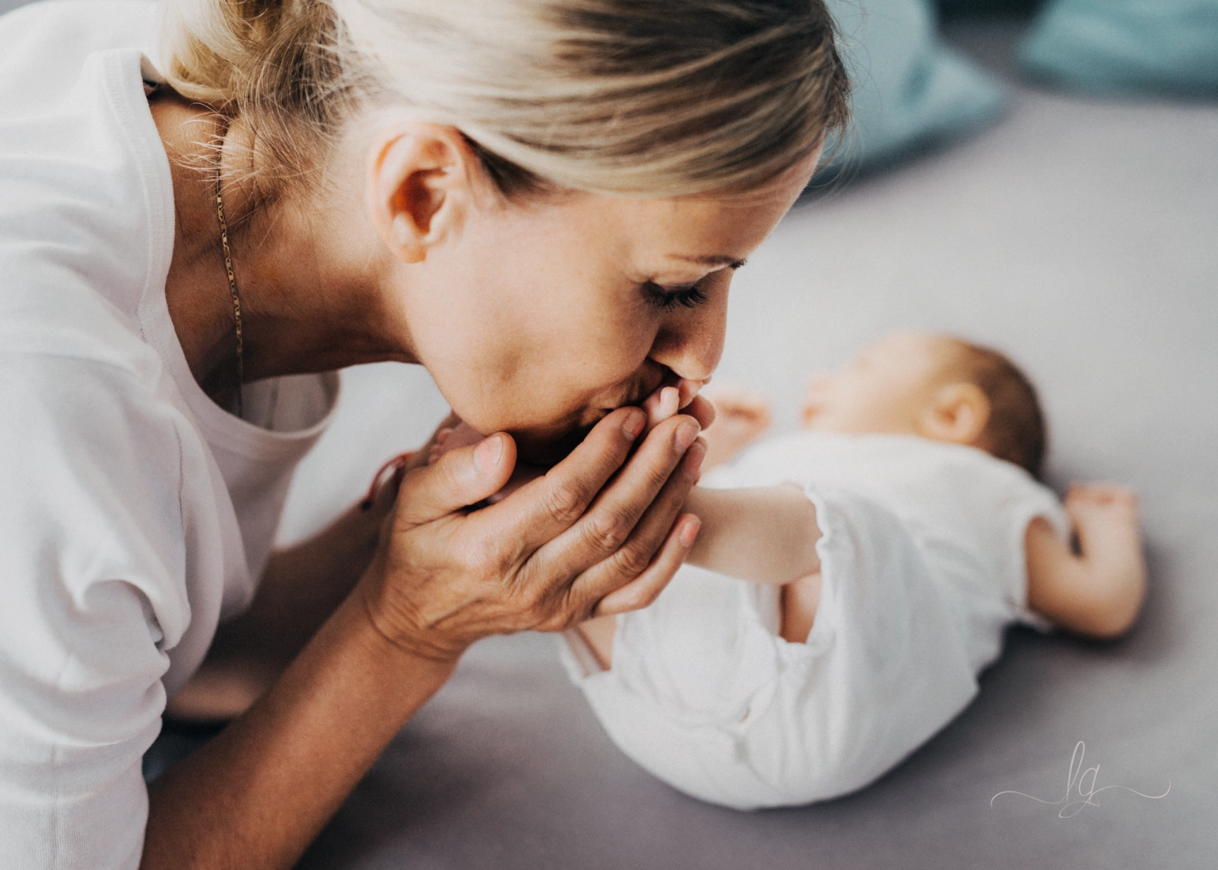A close-up photo of a grandmother gently kissing the foot of a newborn lying on its back.