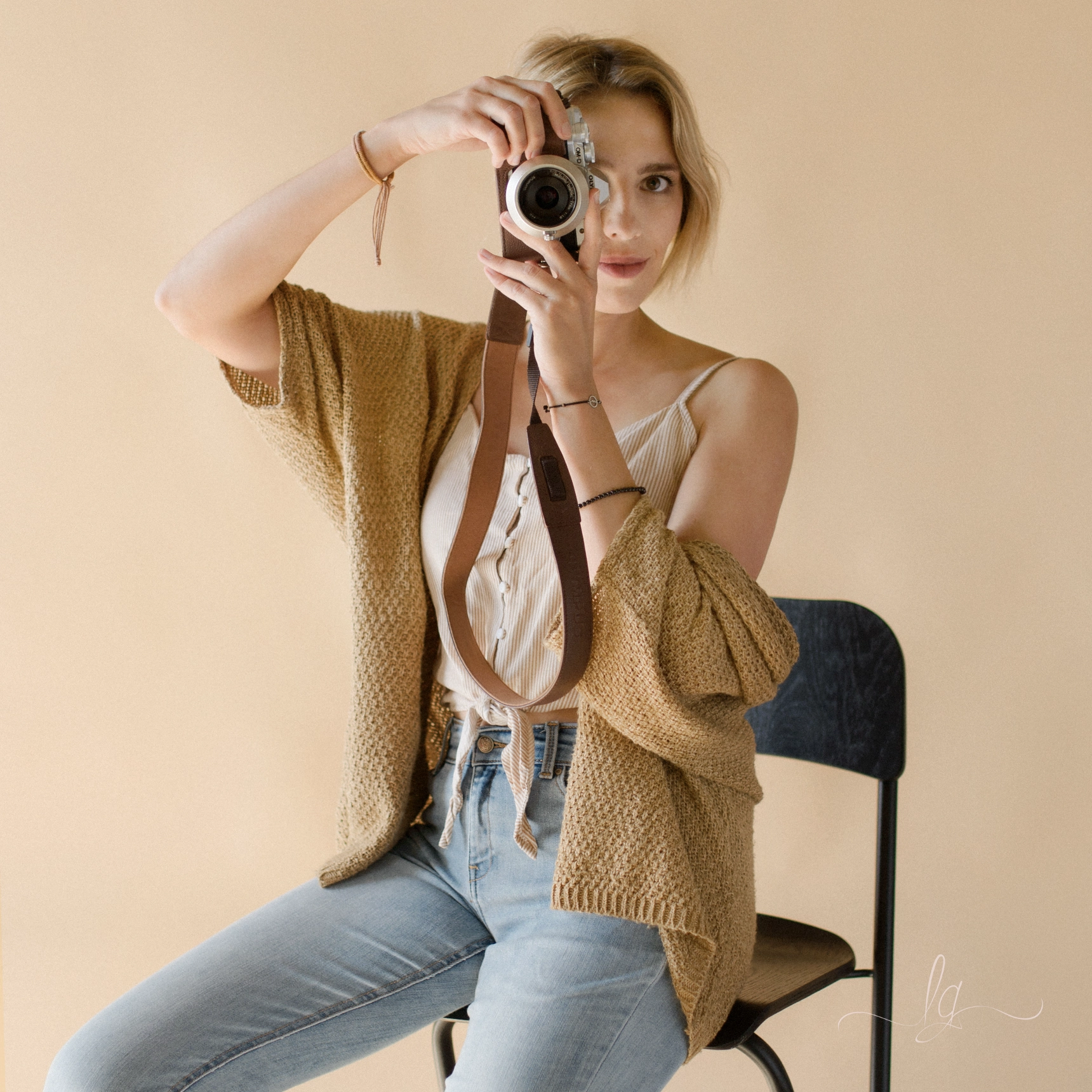 Photographer Lucy Grossmann with a vintage camera in a beige cardigan and jeans.