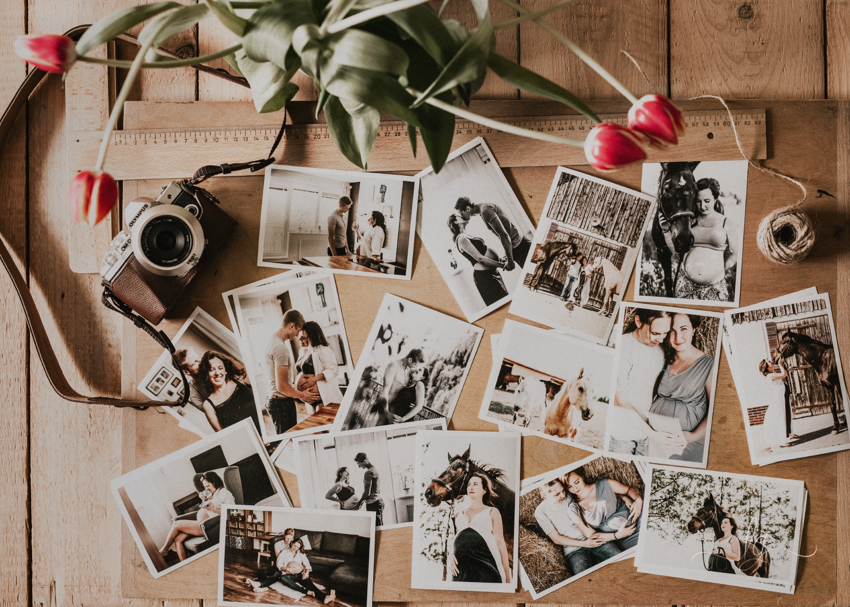 A warm, rustic flat lay featuring numerous printed photographs from a maternity photoshoot, interspersed with a classic camera, craft twine, and fresh tulips, evoking cherished memories.