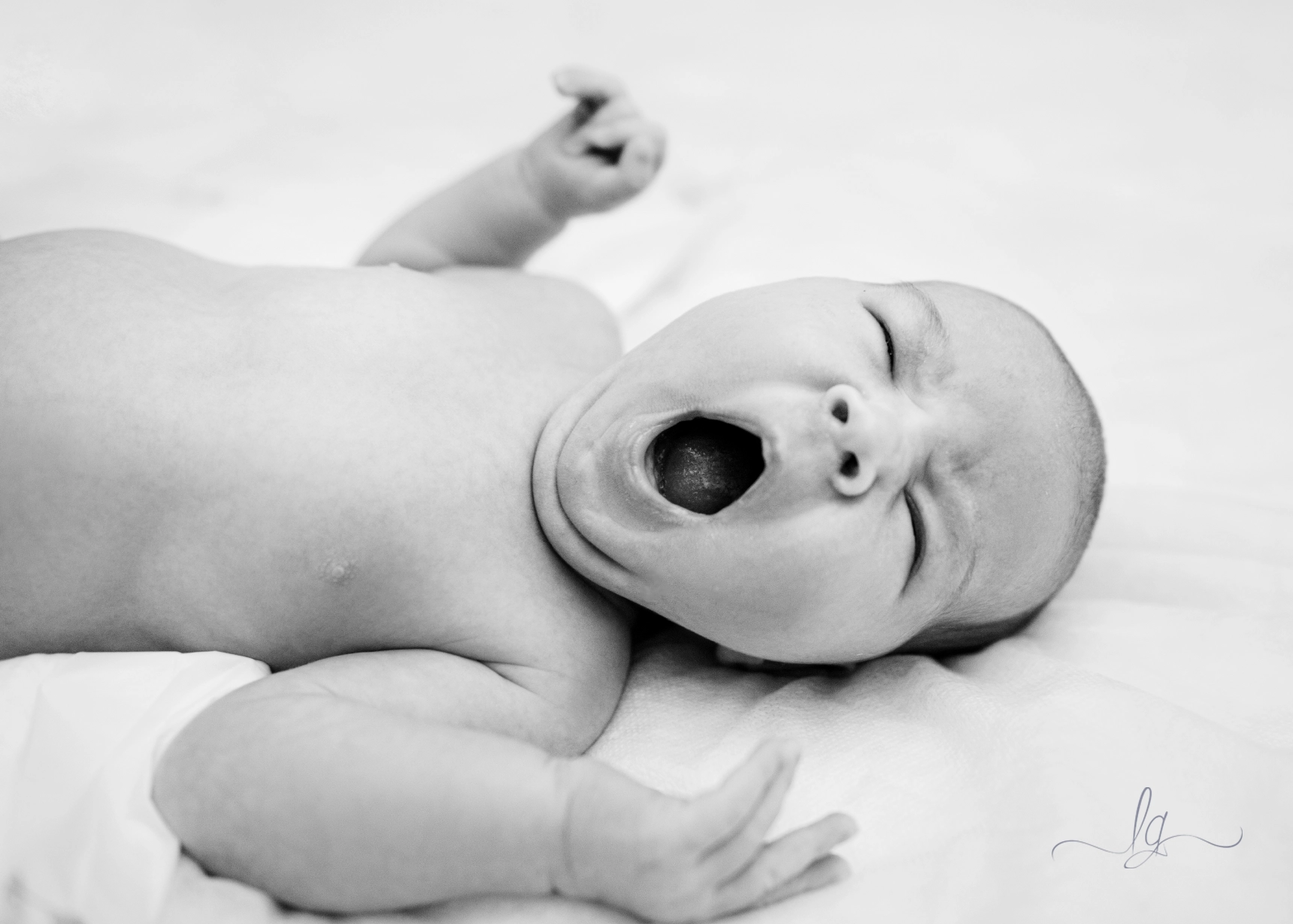 A charming BW newborn portrait: A baby yawning widely on white surface, capturing authentic newborn moment.