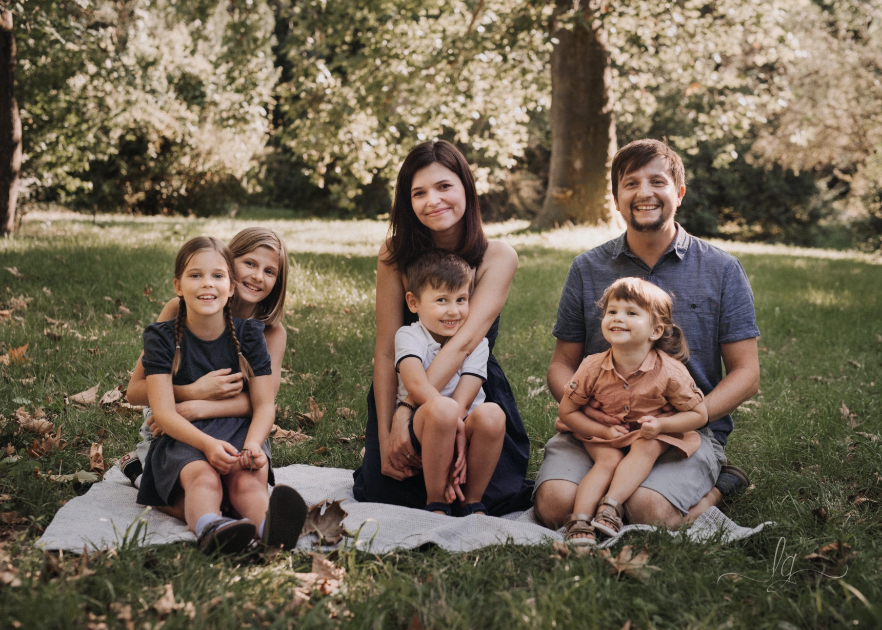 A joyful outdoor family portrait: A family of six, parents and four children, kneeling and sitting on blanket in sunny park.