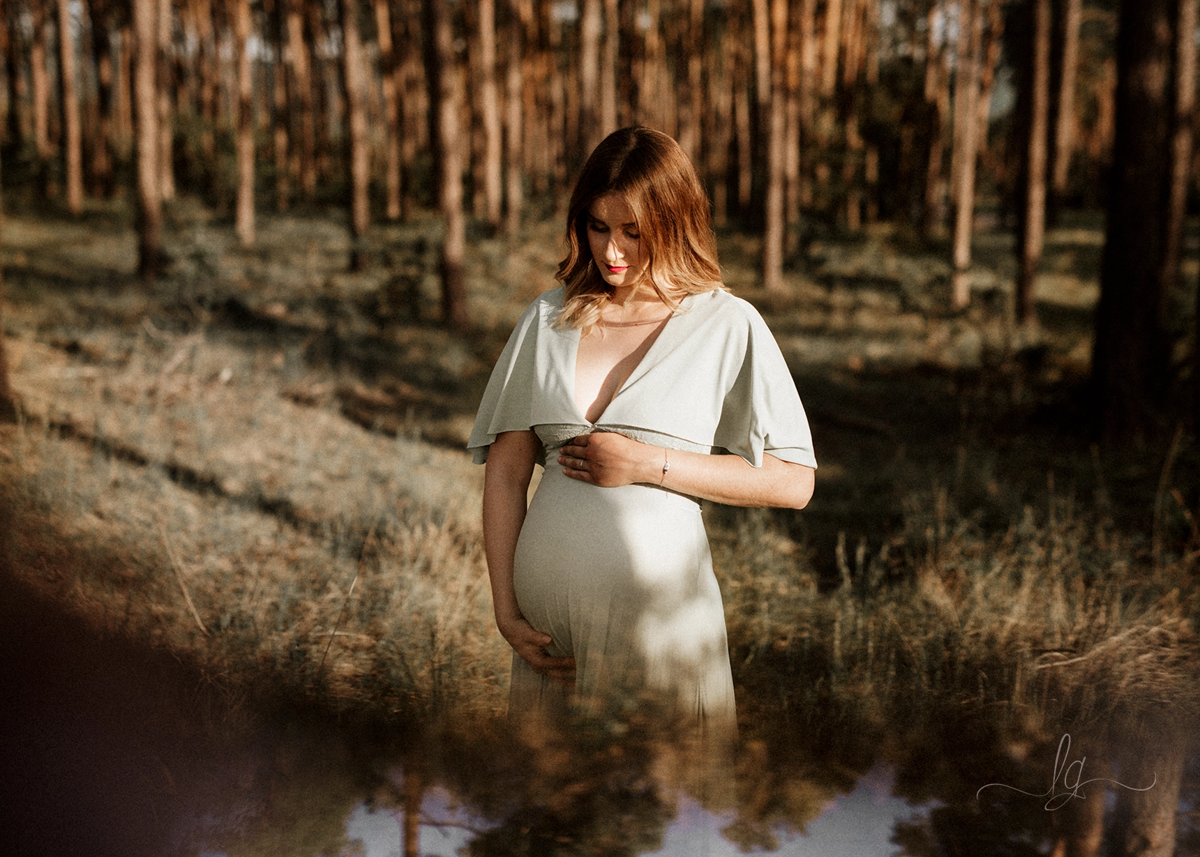 Detailní portrét těhotné ženy v mátových šatech v přírodě při západu slunce.